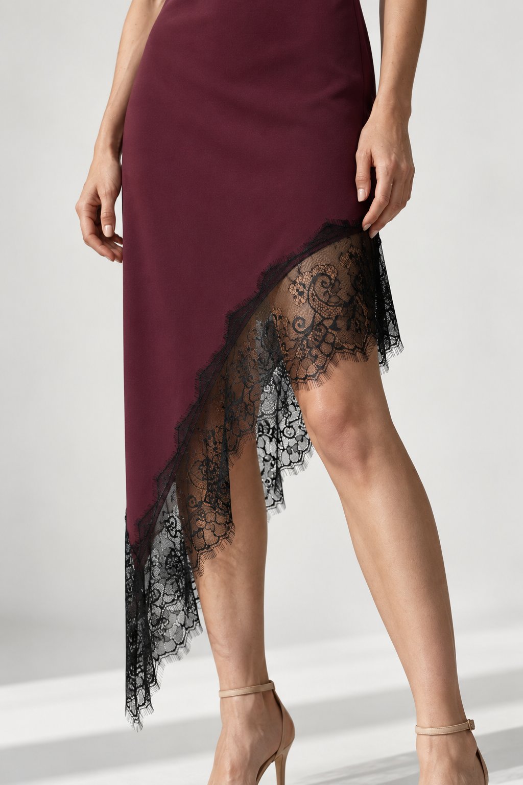 Détail de la robe asymétrique dentelle Bretelles fines Tissu extensible bordeaux, montrant la dentelle raffinée sur le bas.