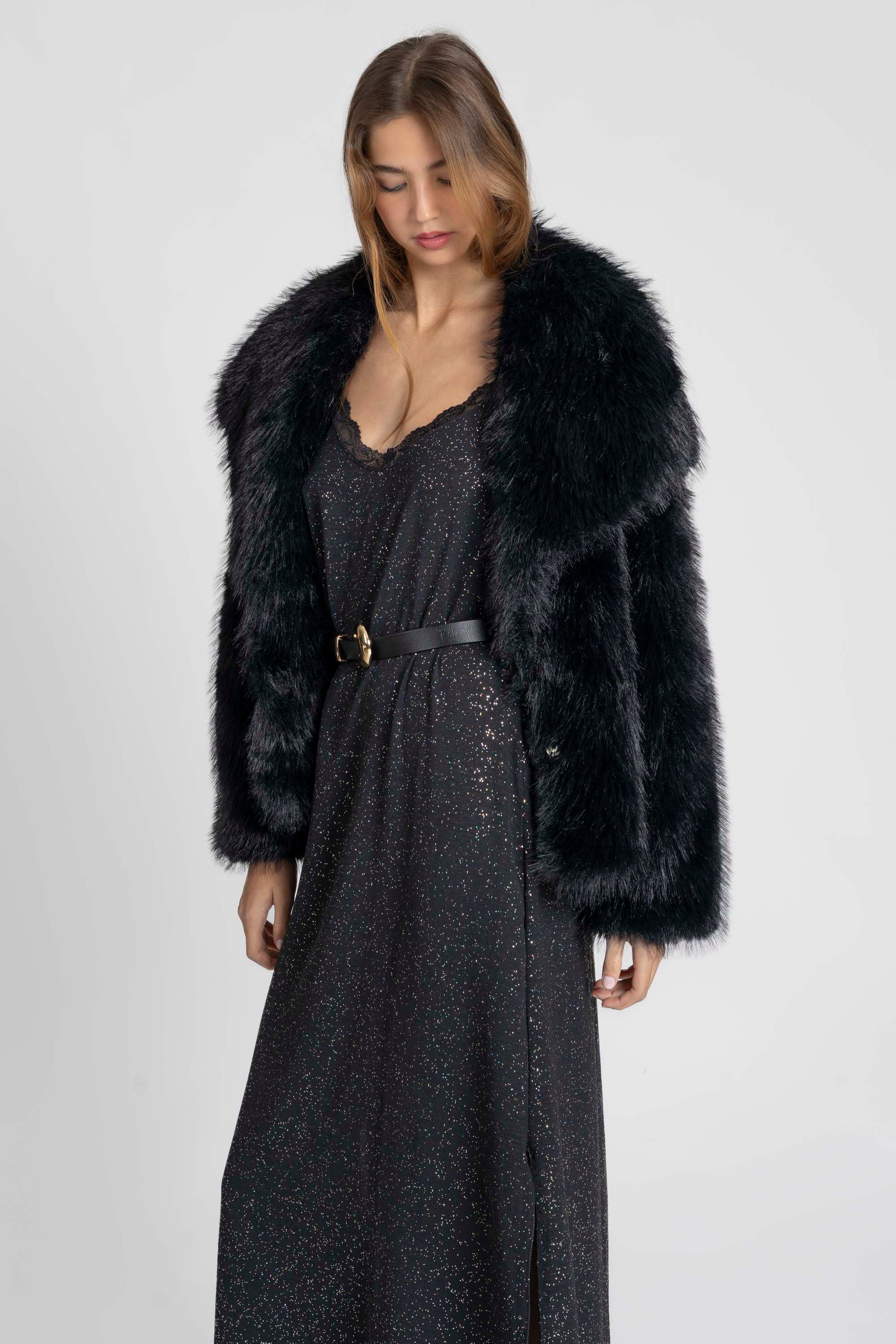 Femme dans une robe fluide noire à fines bretelles soirée, associée à un manteau en fourrure, illustrant un look chic avec la robe longue noire brillante.