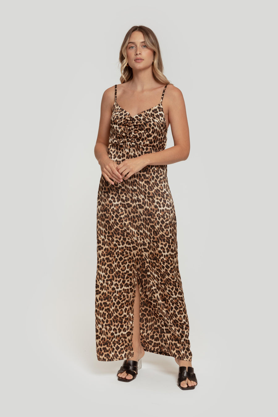 Femme posant en robe longue satinée léopard, révélant une fente élégante, idéale pour un look chic et moderne.