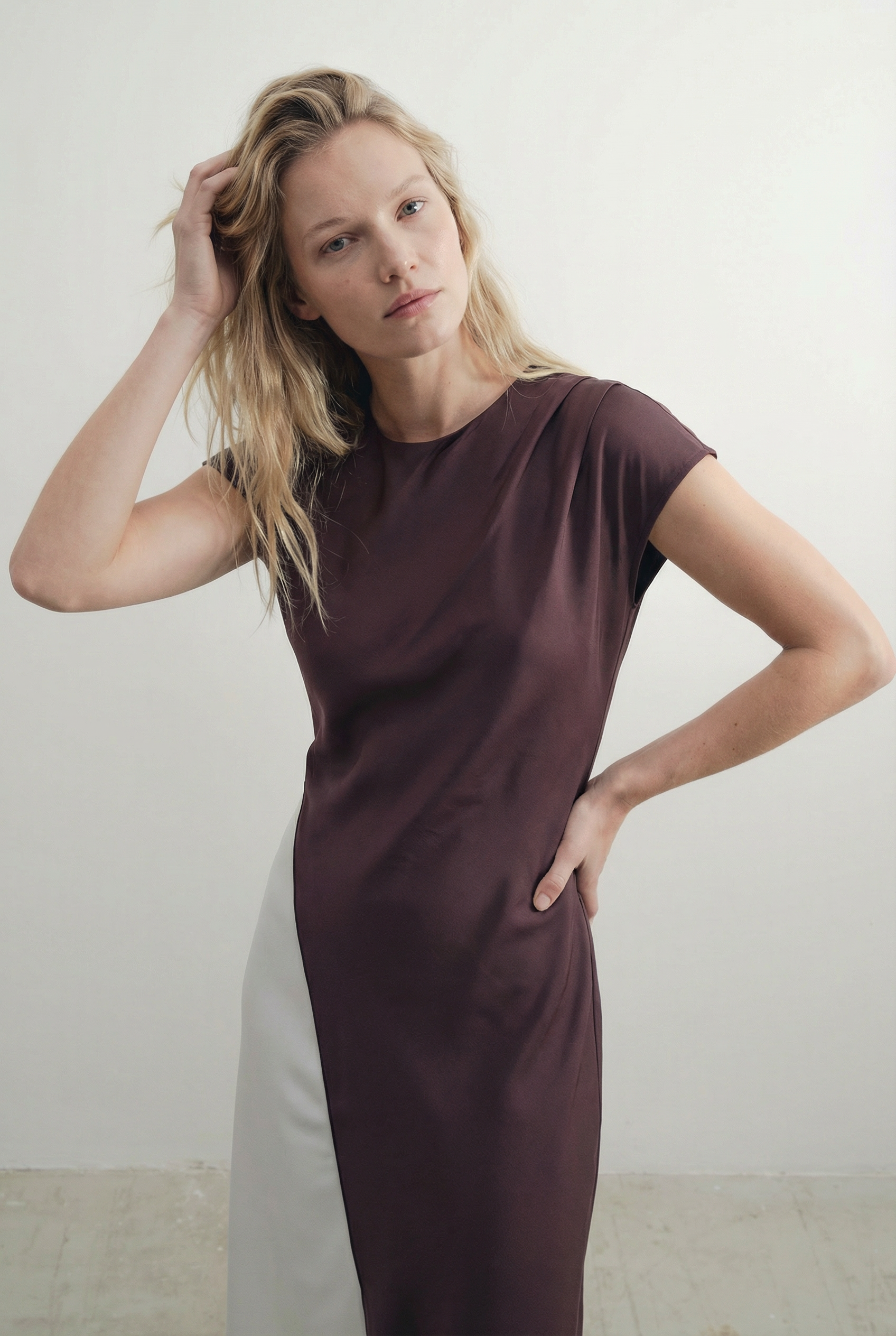 Détail rapproché d'une femme ajustant sa robe midi marron élégante, accentuant les caractéristiques de la robe midi combinée à col rond.