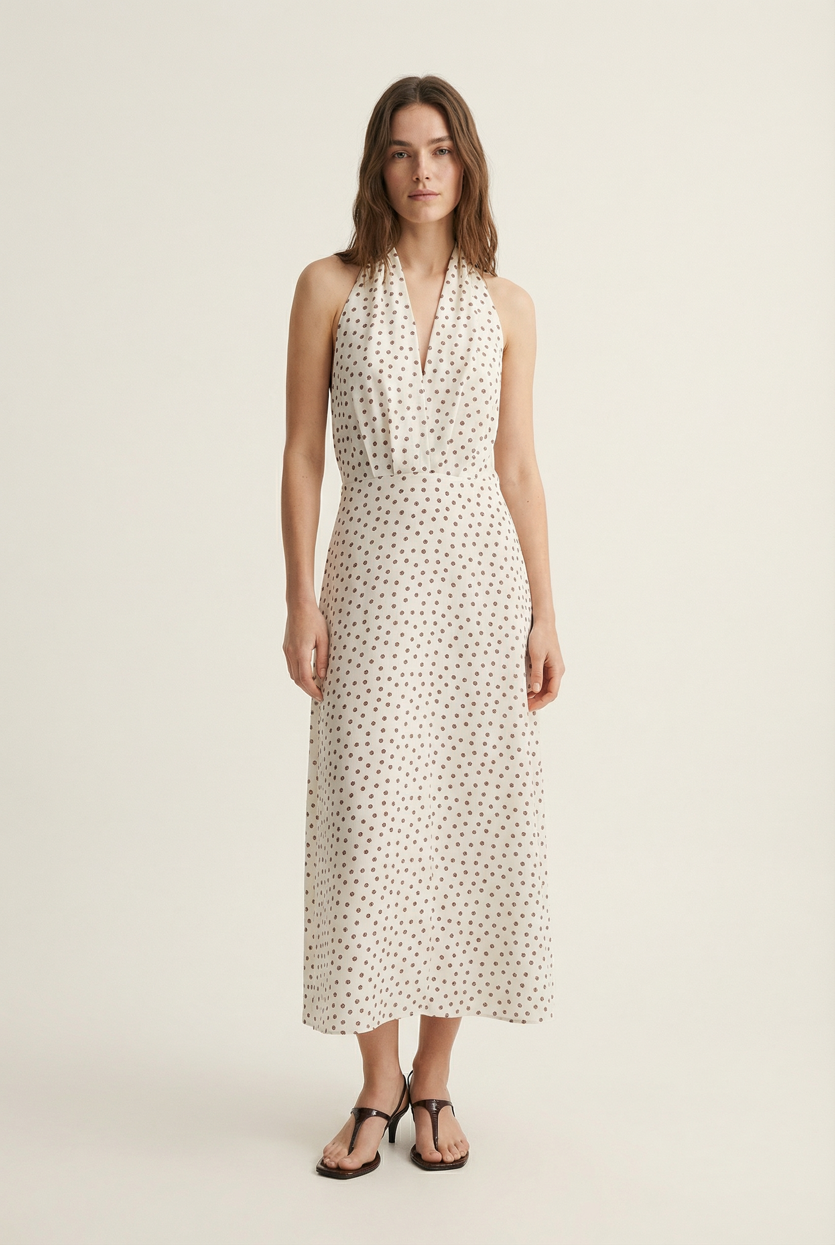 Femme affichant une robe midi imprimée écru à pois, col halter décolleté plongeant, avec un look chic.