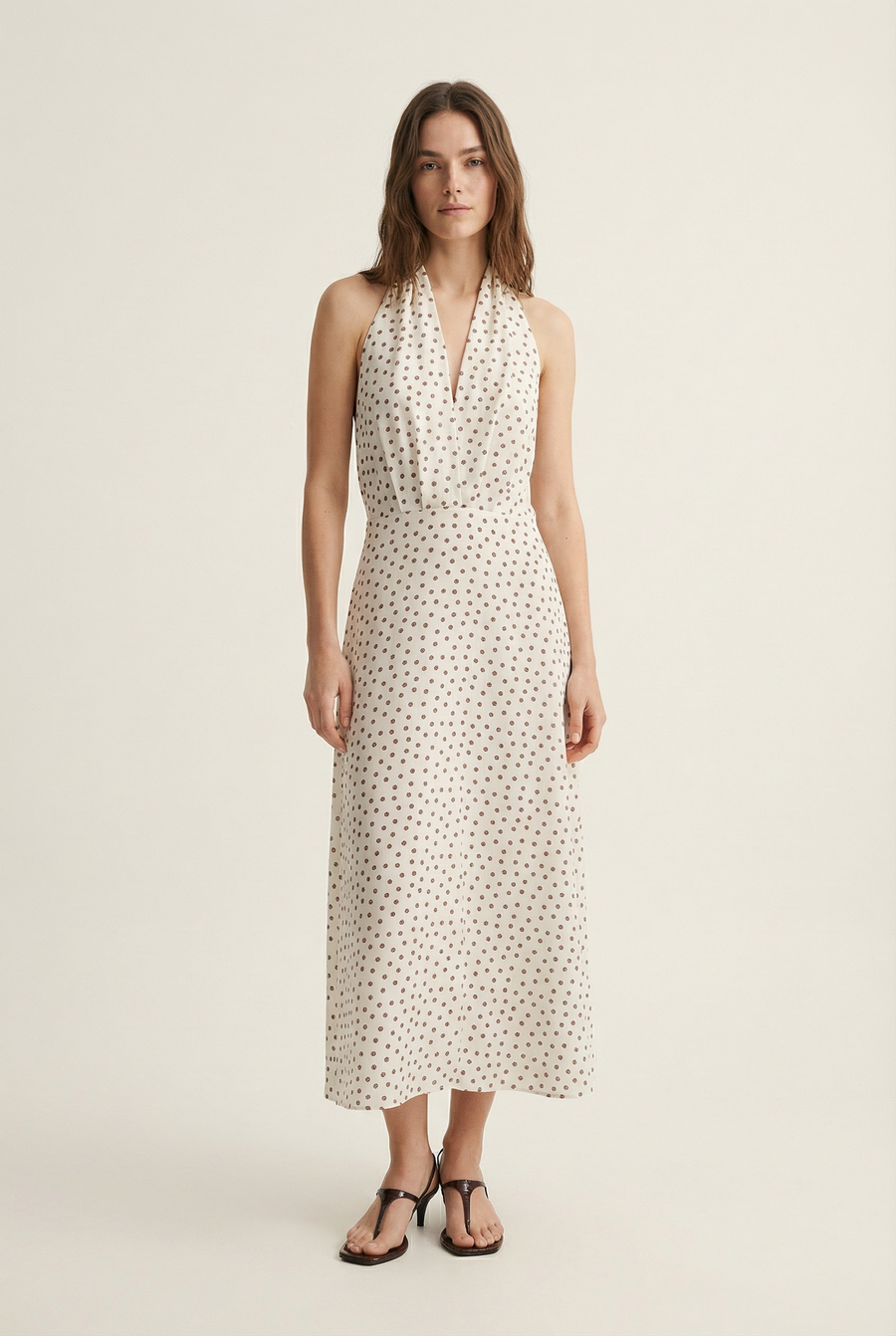 Femme affichant une robe midi imprimée écru à pois, col halter décolleté plongeant, avec un look chic.