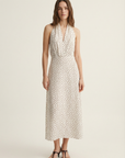 Femme affichant une robe midi imprimée écru à pois, col halter décolleté plongeant, avec un look chic.