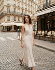 Femme marchant dans une robe midi imprimée écru à pois, col halter décolleté plongeant, dans une rue parisienne.