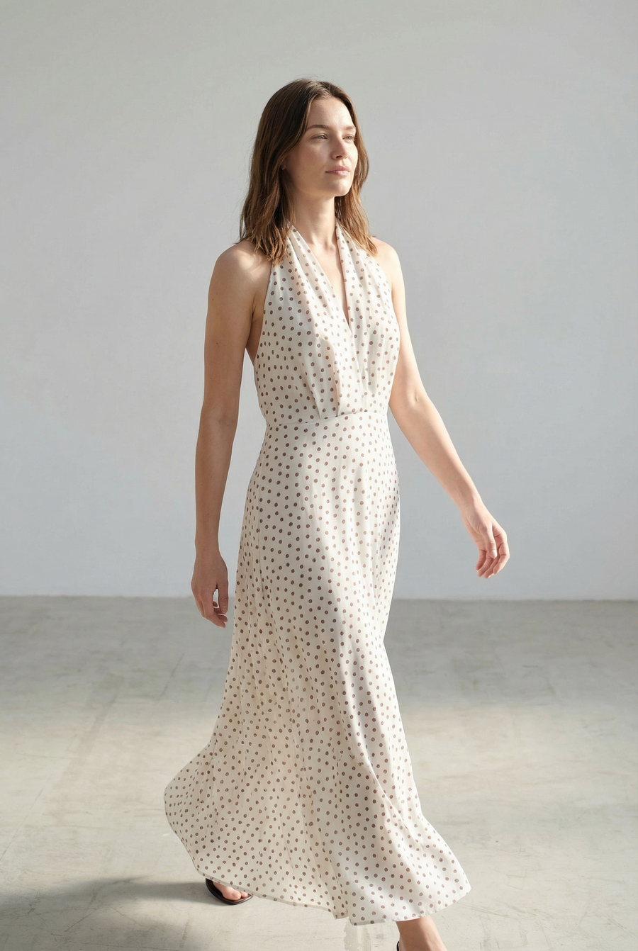 Femme en robe midi imprimée écru à pois, col halter décolleté plongeant, s'avançant avec assurance.