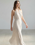 Femme en robe midi imprimée écru à pois, col halter décolleté plongeant, s'avançant avec assurance.
