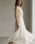 Femme en robe midi imprimée écru à pois, col halter décolleté plongeant, se déplaçant avec élégance.