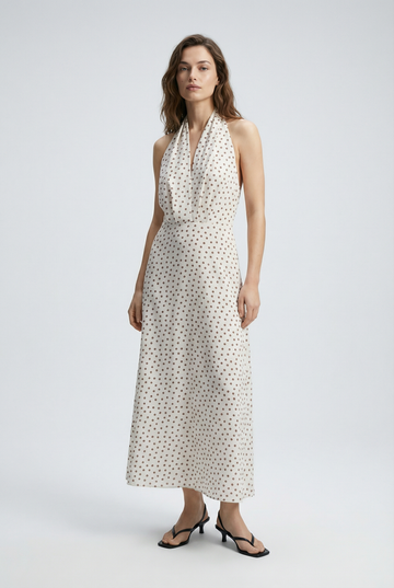 Femme élégante dans une robe midi imprimée écru à pois, col halter décolleté plongeant, sur fond clair.