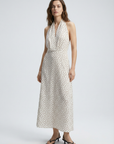 Femme élégante dans une robe midi imprimée écru à pois, col halter décolleté plongeant, sur fond clair.