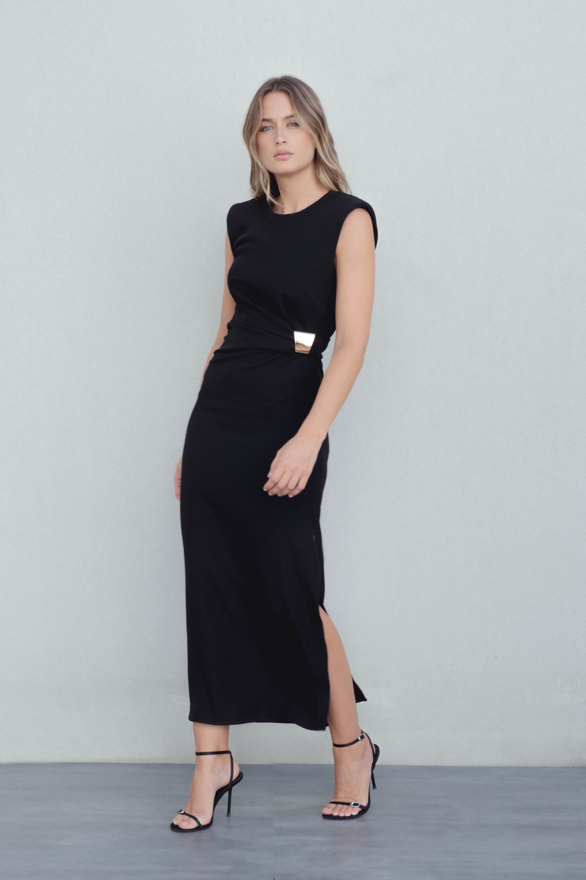 Vue de face de la robe midi noire élégante avec applique dorée, portée par un mannequin, mettant en valeur la coupe moderne.