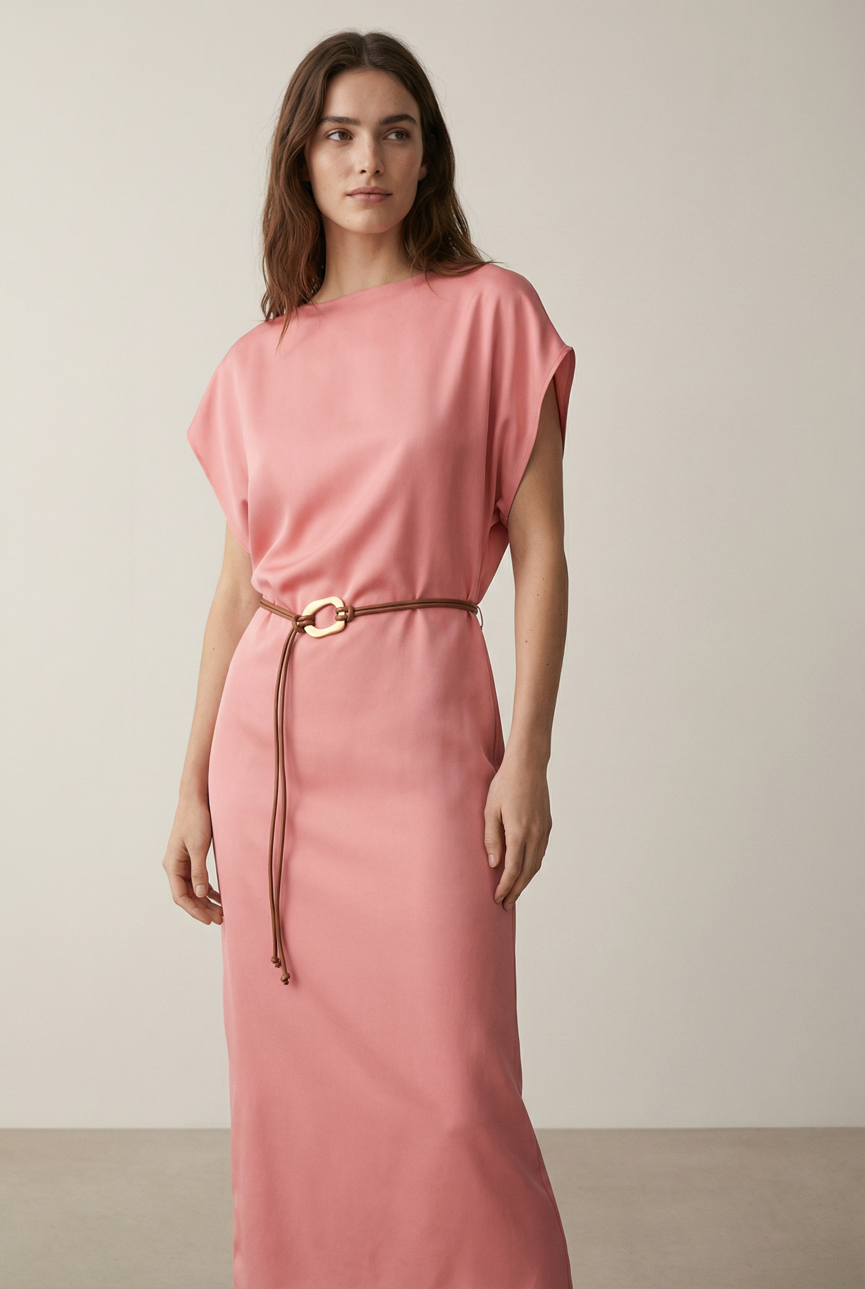 Femme debout dans une robe midi satinée avec ceinture fine couleur rose, mélangeant élégance et confort.