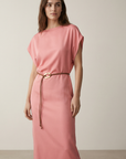 Femme debout dans une robe midi satinée avec ceinture fine couleur rose, mélangeant élégance et confort.