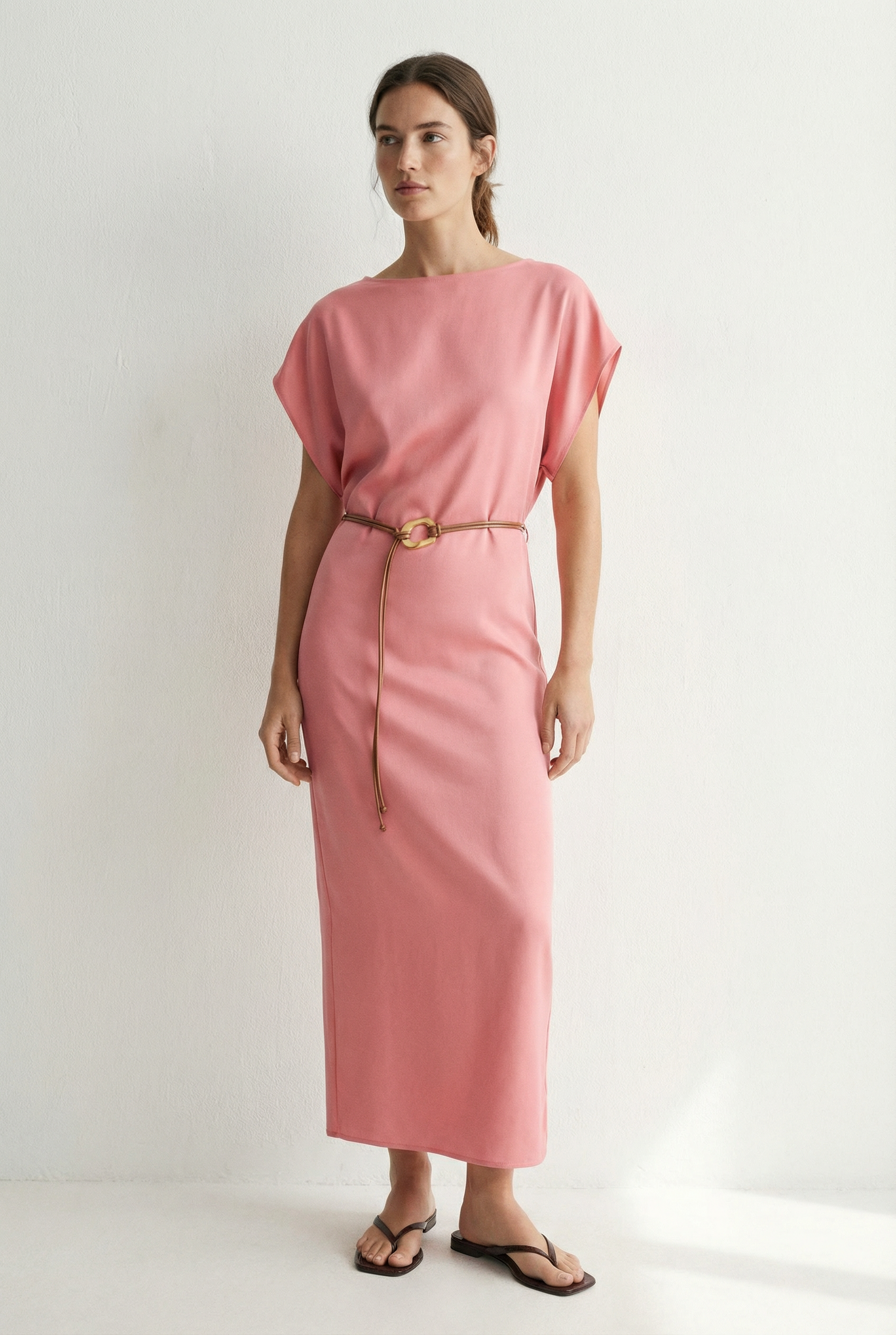 Femme souriante dans une robe midi satinée avec ceinture fine couleur rose, mettant en avant un look naturel.