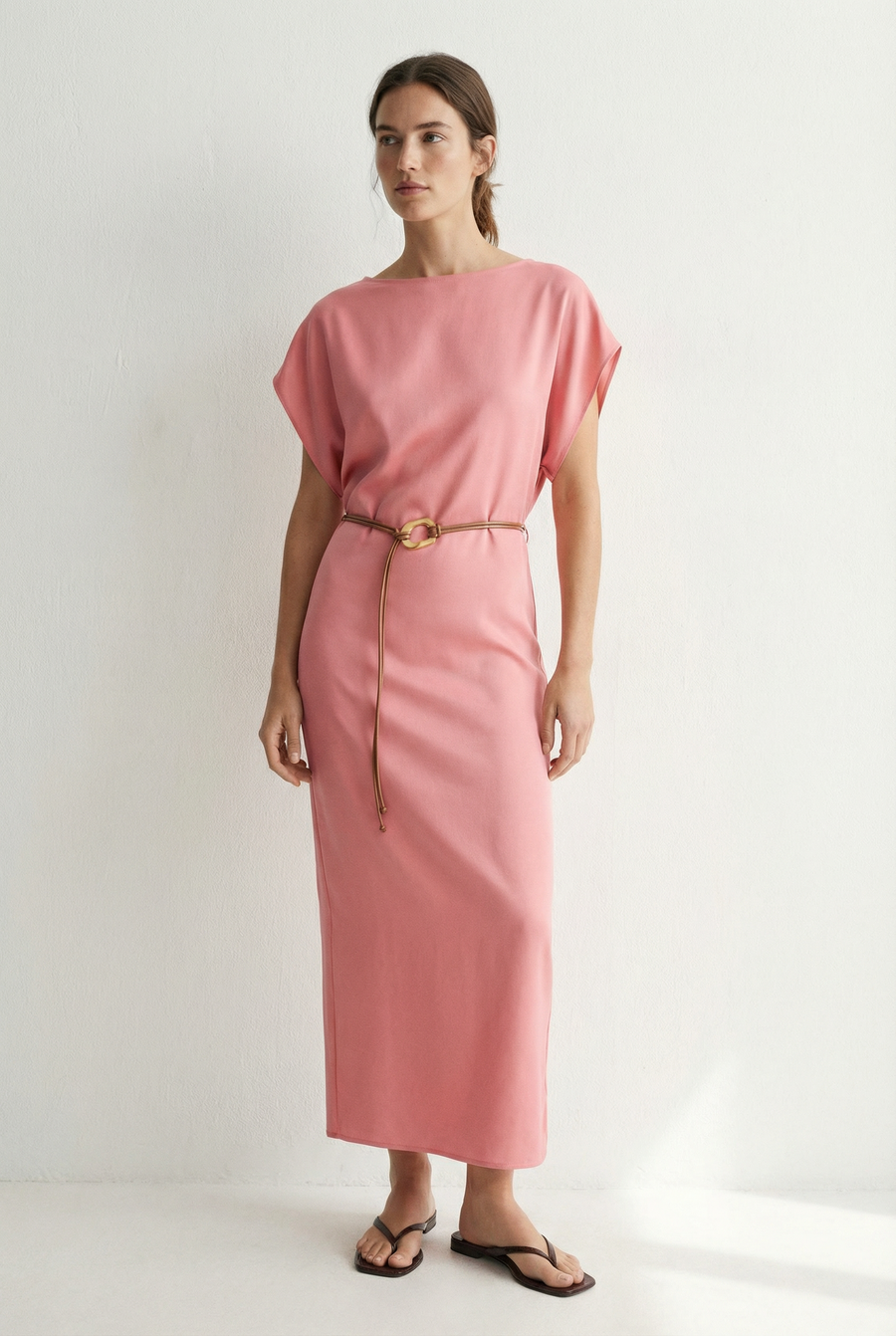 Femme souriante dans une robe midi satinée avec ceinture fine couleur rose, mettant en avant un look naturel.