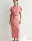 Femme souriante dans une robe midi satinée avec ceinture fine couleur rose, mettant en avant un look naturel.
