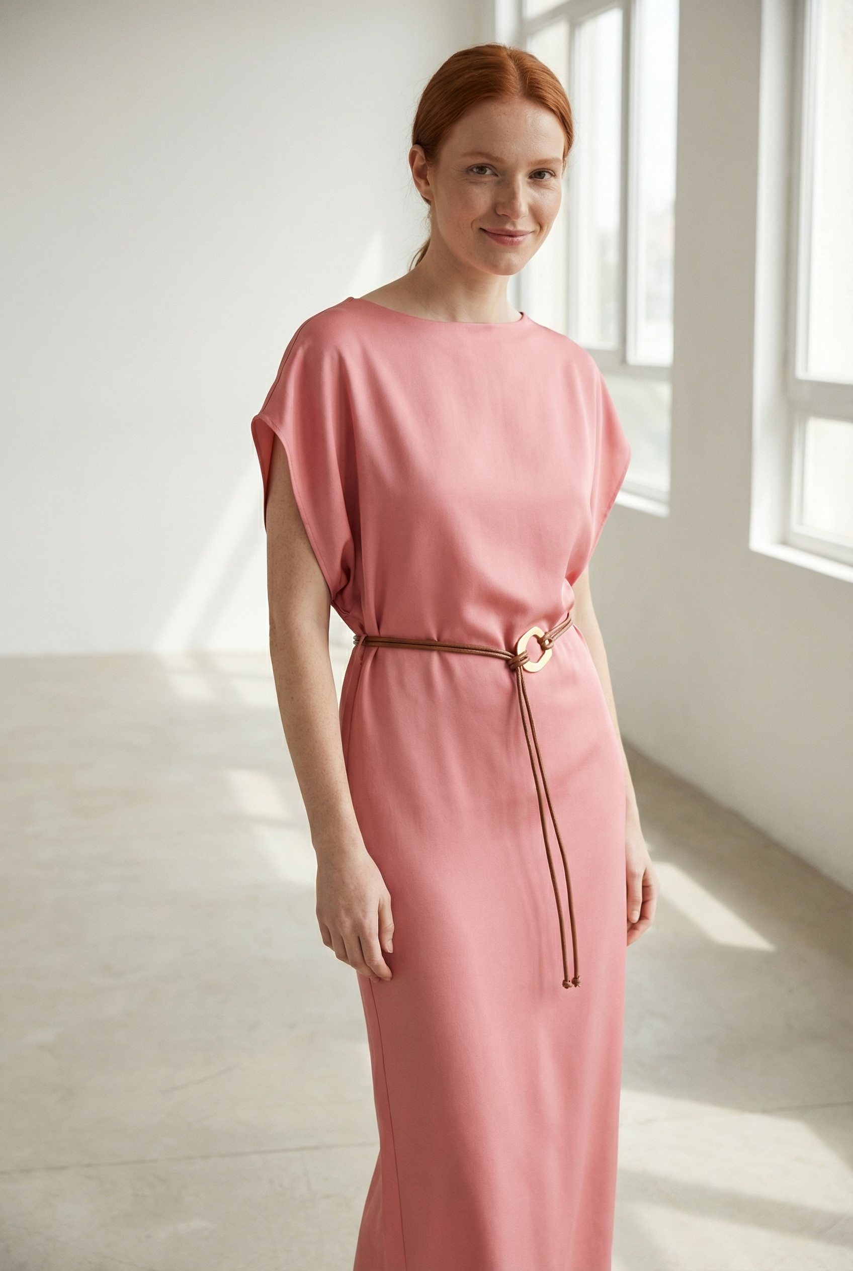 Femme souriante dans une robe midi satinée avec ceinture fine couleur rose, captivant l'attention avec un look lumineux.
