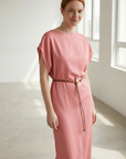 Femme souriante dans une robe midi satinée avec ceinture fine couleur rose, captivant l'attention avec un look lumineux.