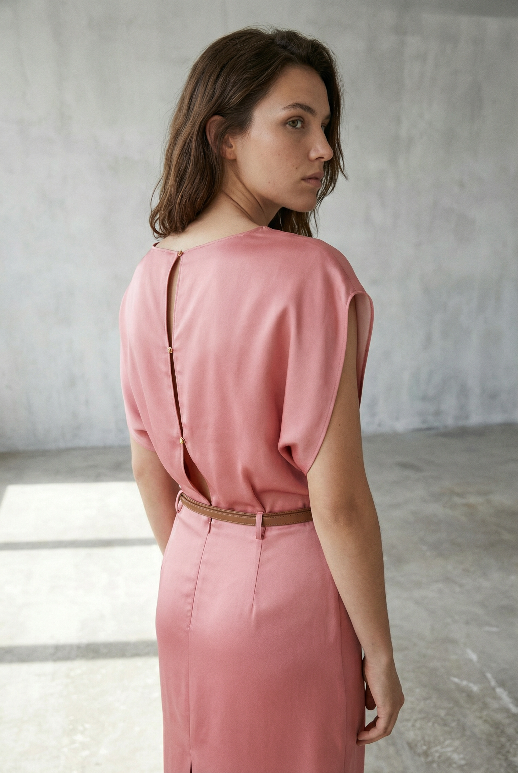 Détail arrière d'une femme en robe midi satinée avec ceinture fine couleur rose, soulignant le design élégant.