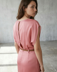 Détail arrière d'une femme en robe midi satinée avec ceinture fine couleur rose, soulignant le design élégant.