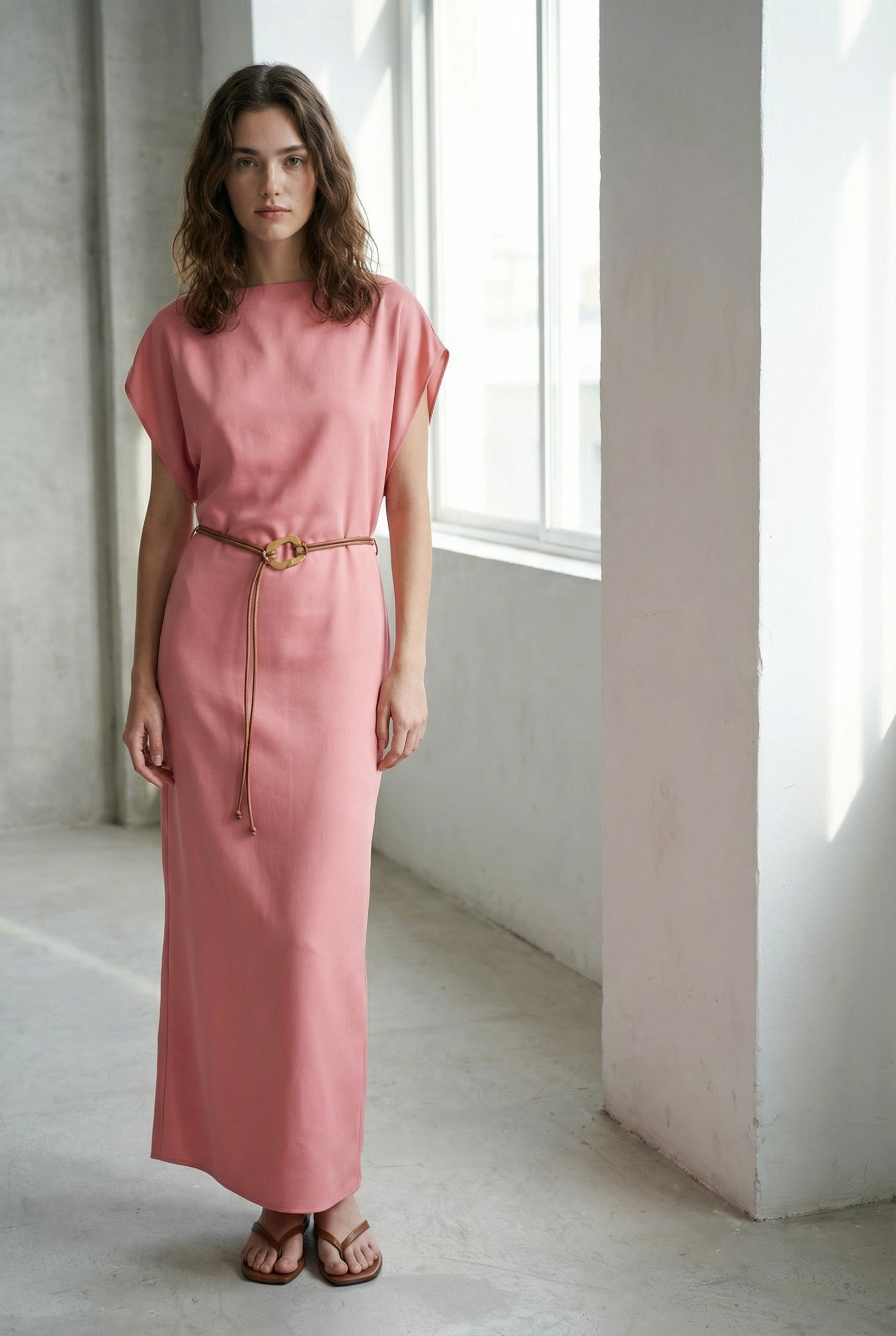 Femme posant dans une lumière douce, portant une robe midi satinée avec ceinture fine couleur rose.