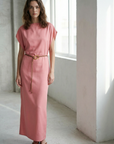 Femme posant dans une lumière douce, portant une robe midi satinée avec ceinture fine couleur rose.
