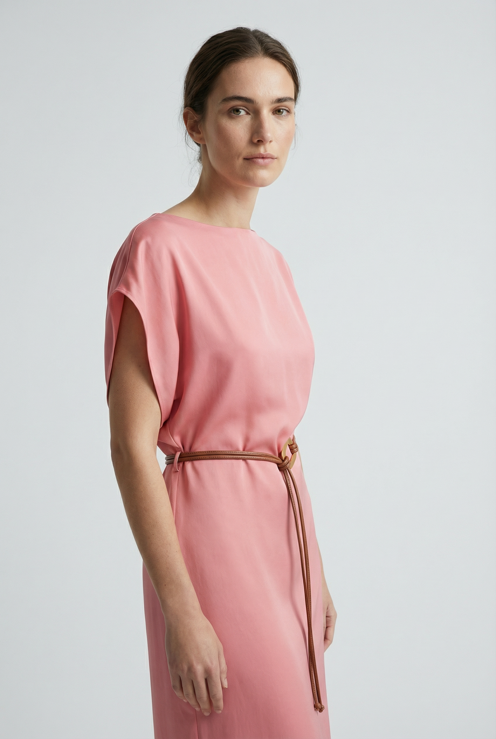 Portrait de femme en close-up dans une robe midi satinée avec ceinture fine couleur rose, montrant une allure délicate.