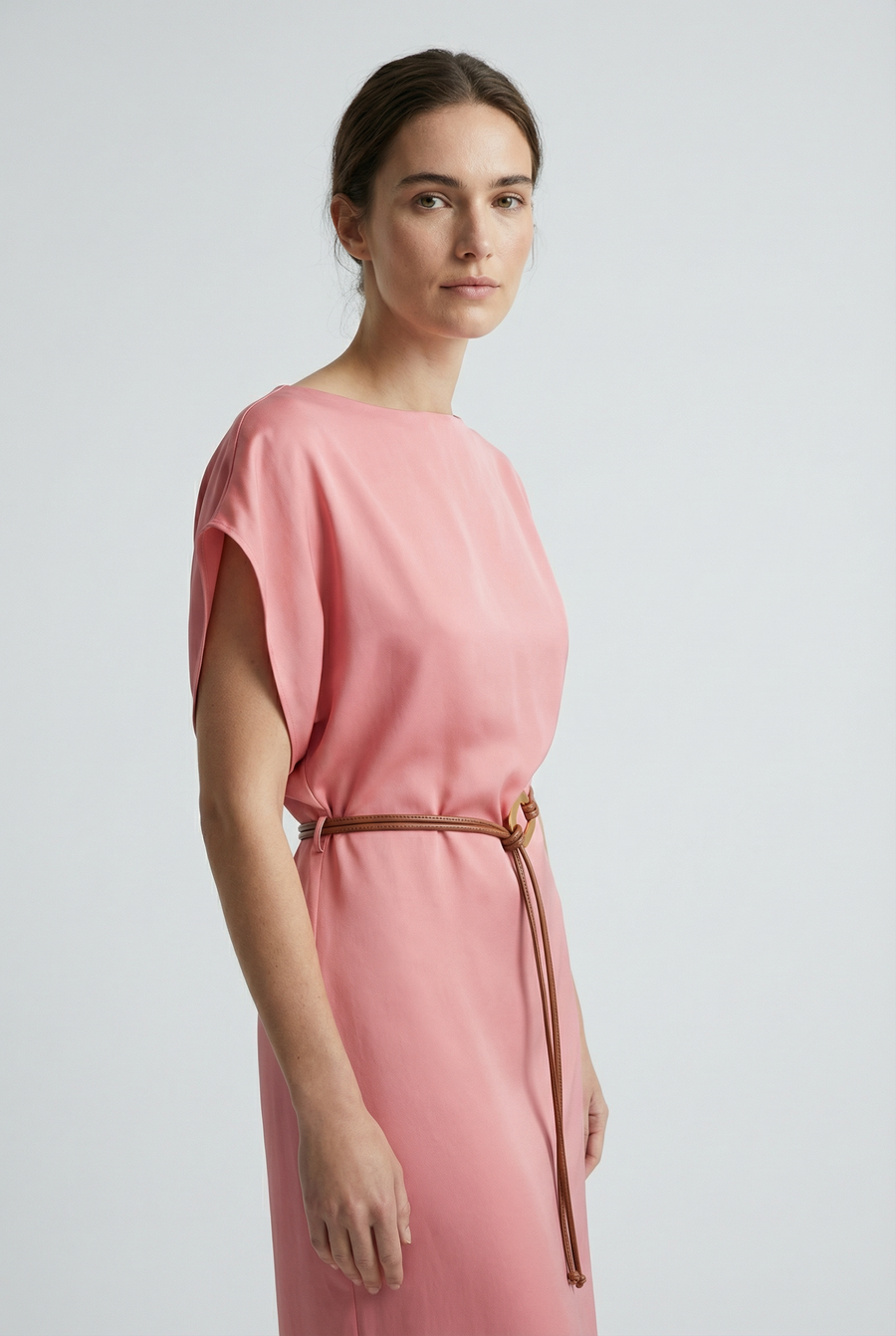 Portrait de femme en close-up dans une robe midi satinée avec ceinture fine couleur rose, montrant une allure délicate.
