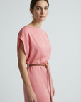 Portrait de femme en close-up dans une robe midi satinée avec ceinture fine couleur rose, montrant une allure délicate.