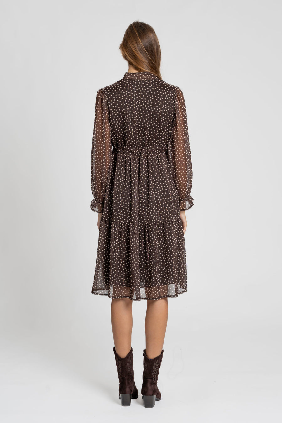Vue arrière d'une femme en robe midi fluide marron imprimée avec des pois, style à cordon et manches longues. Parfaite pour les soirées ou les journées décontractées. Robe pois marron.