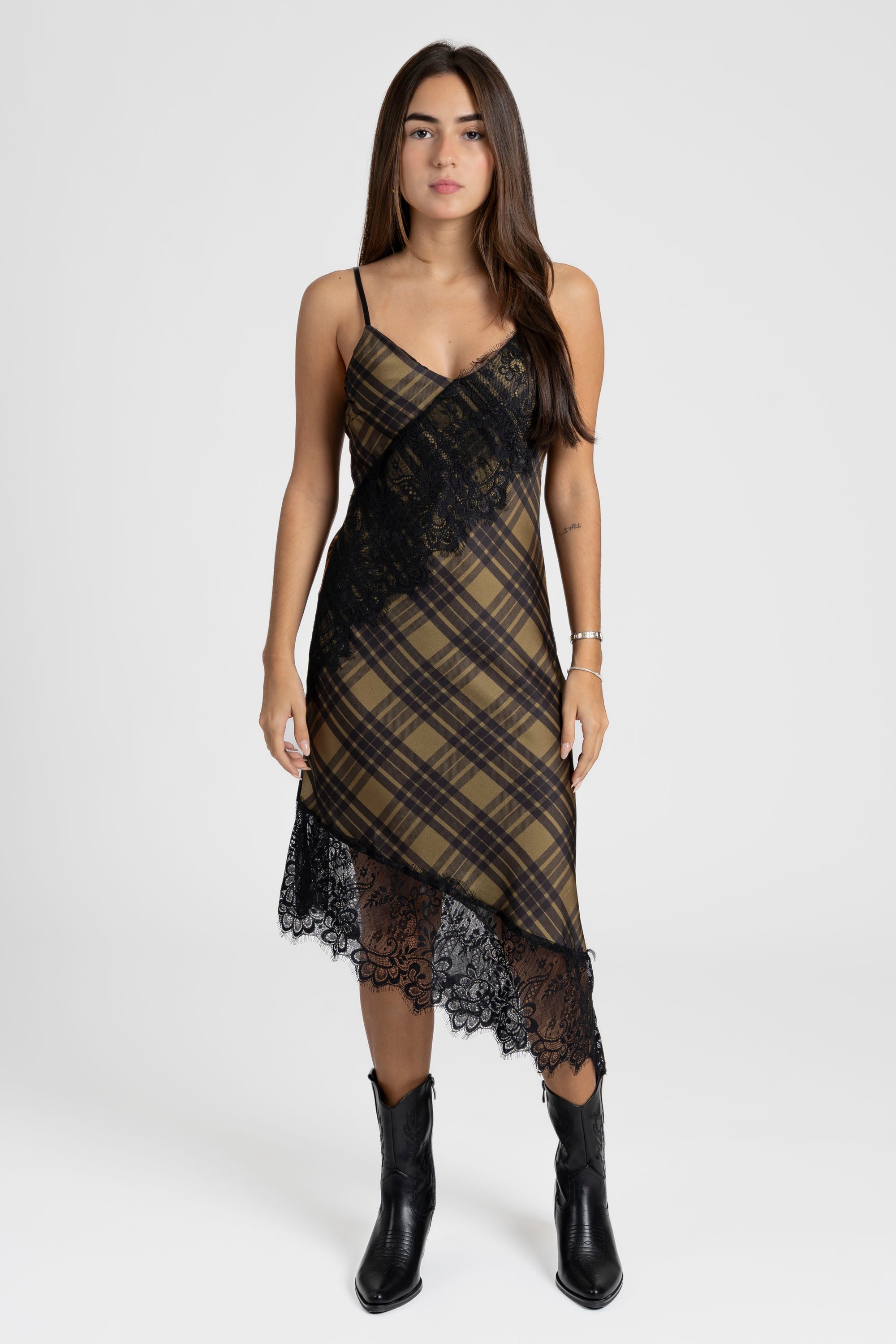 Modèle portant une robe satin asymétrique avec un décolleté en V et dentelle raffinée, au motif à carreaux olive et noir, dans un style chic.