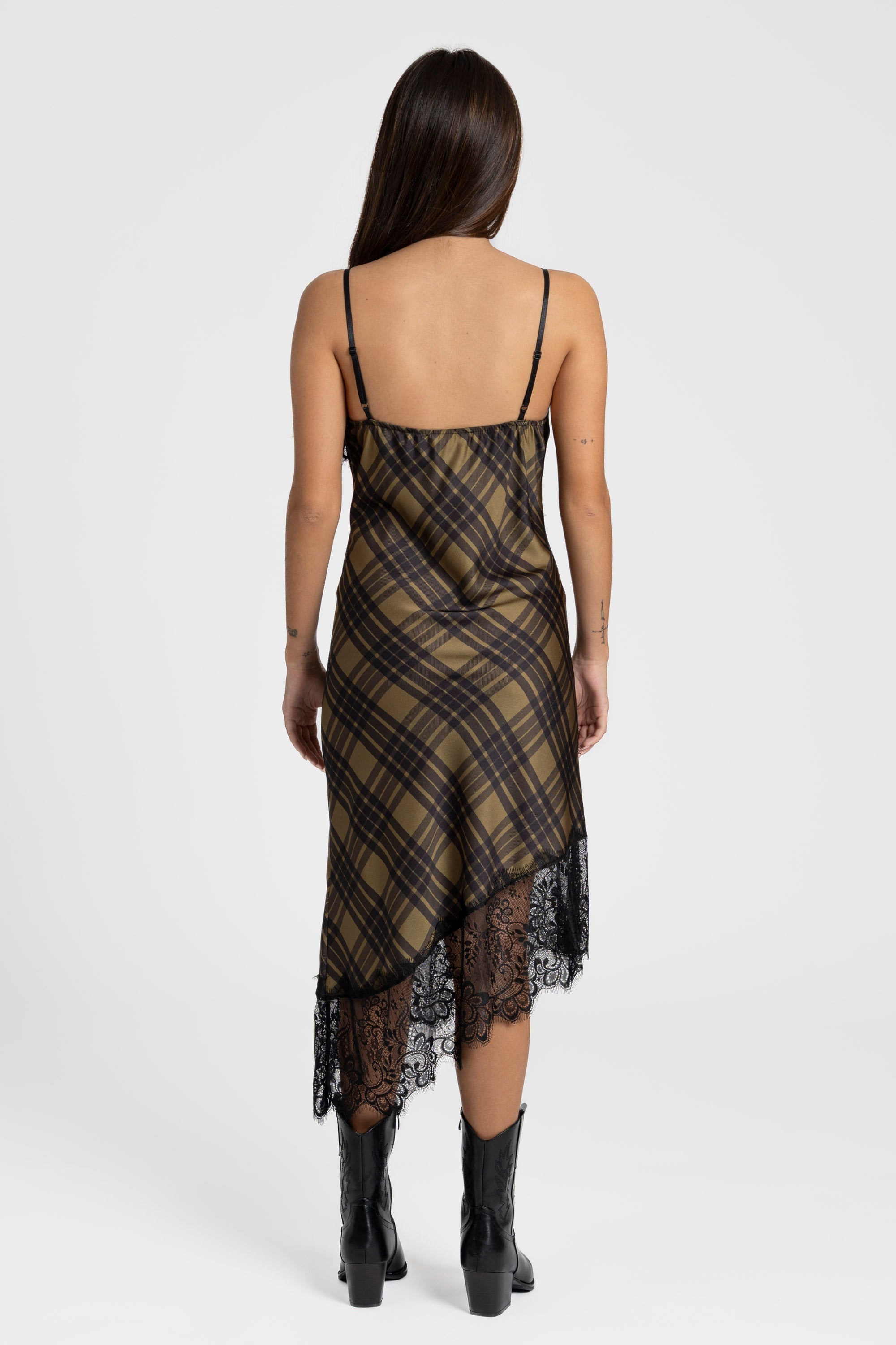 Vue arrière d'une femme portant une robe satin asymétrique avec dentelle, en motif à carreaux olive et noir, accessoirisée avec des bottes.