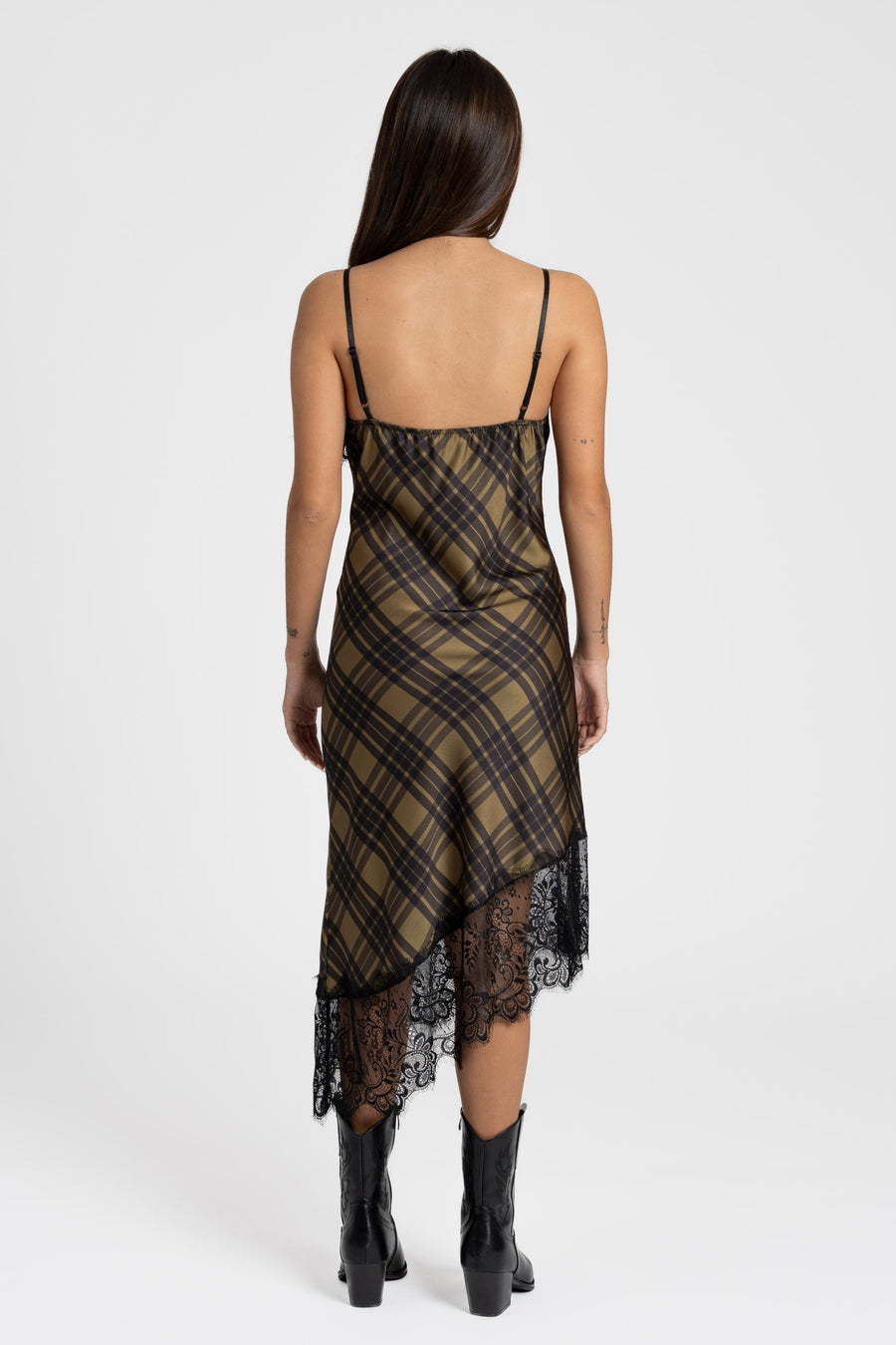 Vue arrière d'une femme portant une robe satin asymétrique avec dentelle, en motif à carreaux olive et noir, accessoirisée avec des bottes.
