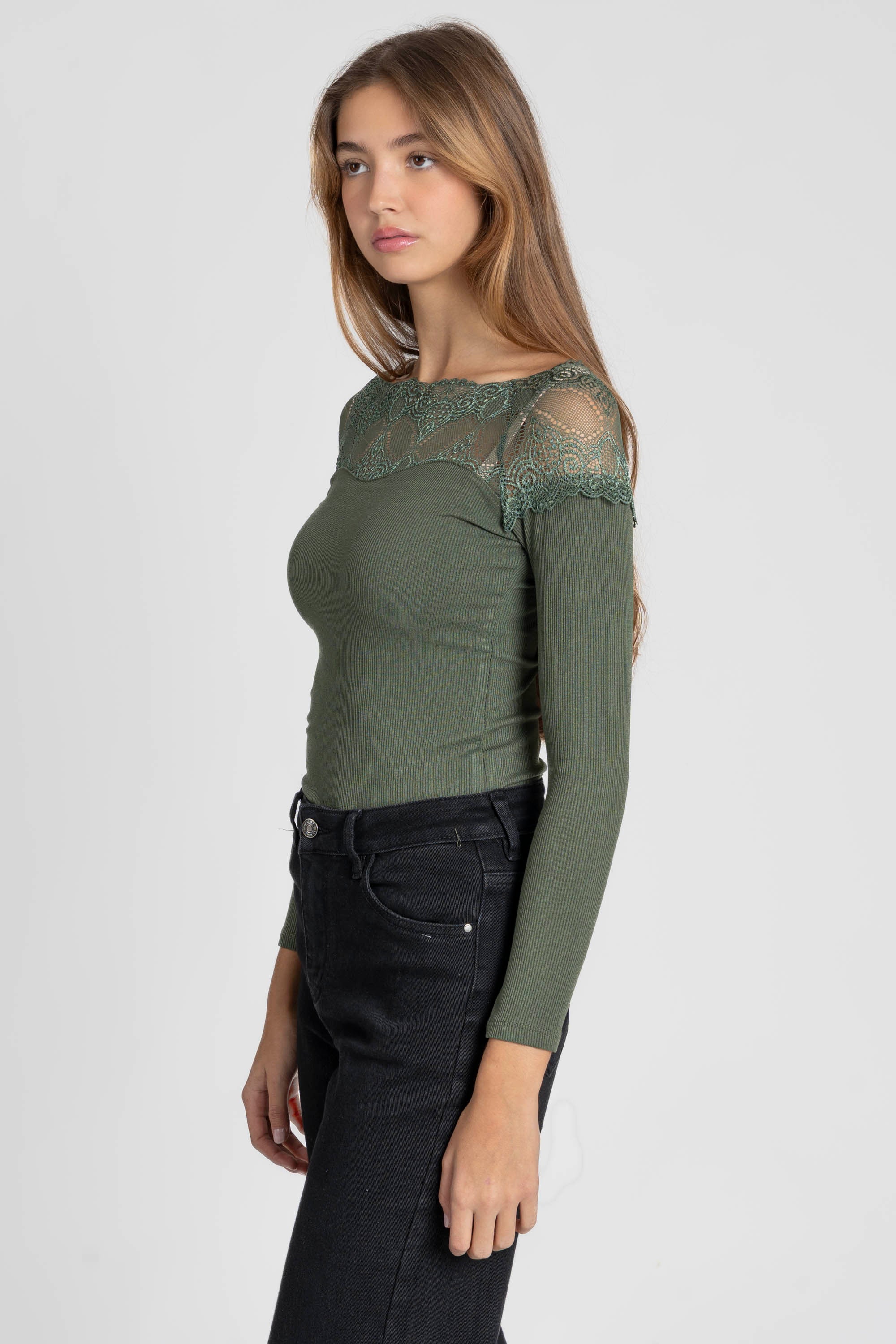 Femme en profil portant un T-shirt dentelle Manches longues vert foncé qui souligne sa silhouette.