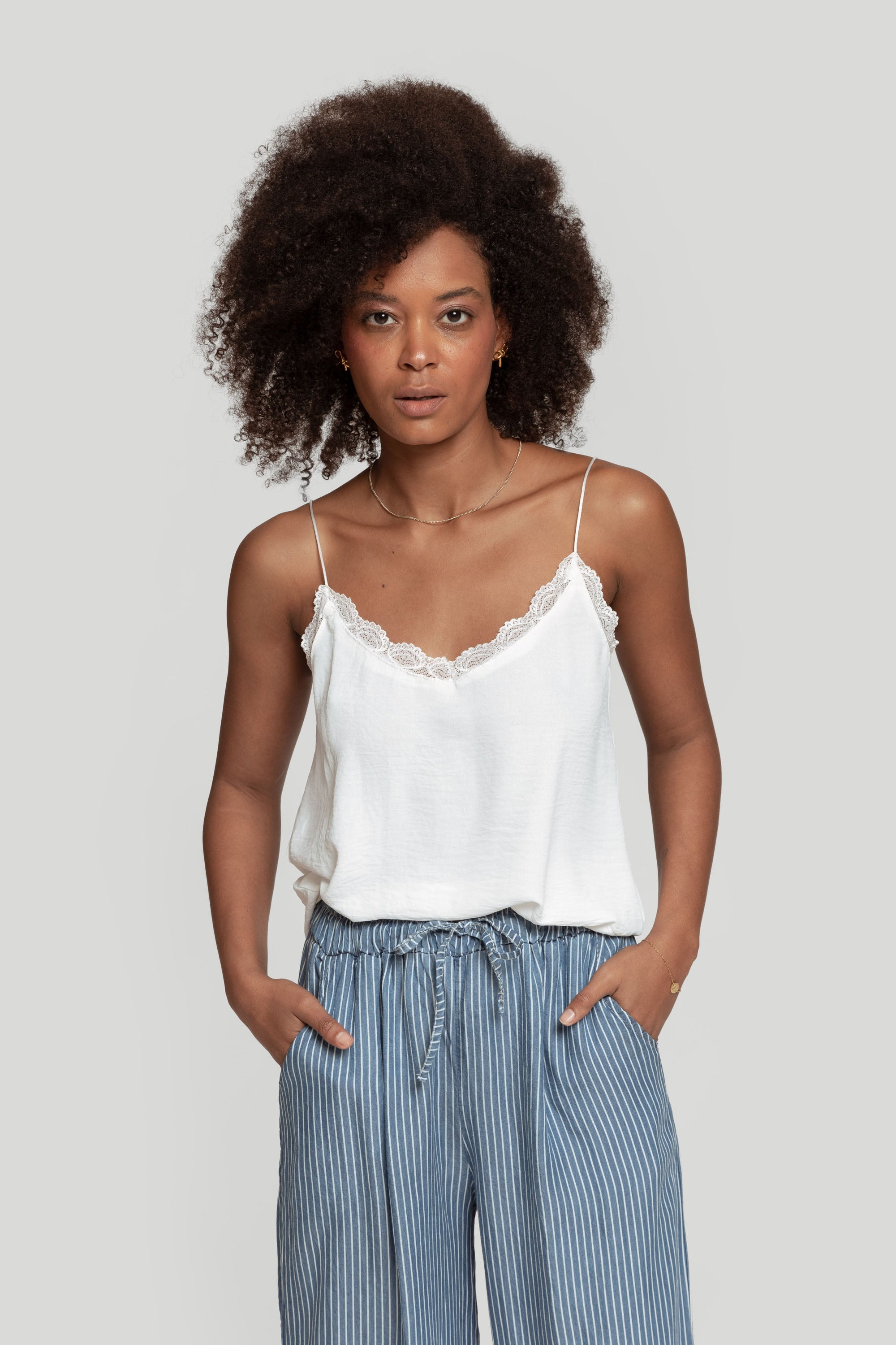 Top en mousseline femme fluide à bretelles avec dentelle blanche, porté par une femme, style moderne et élégant.