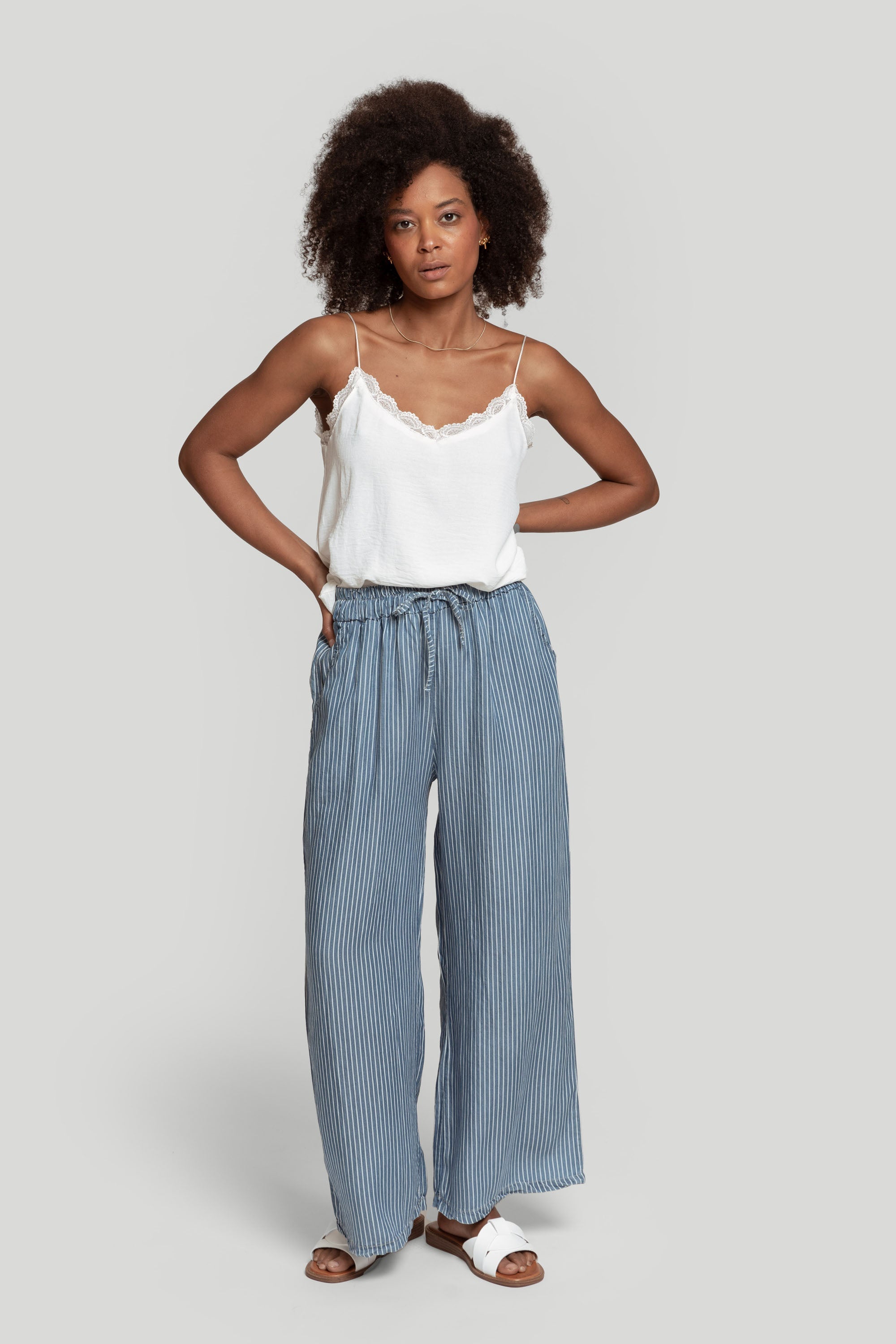 Femme portant un top en mousseline femme fluide à bretelles avec dentelle blanche, associé à un pantalon rayé.