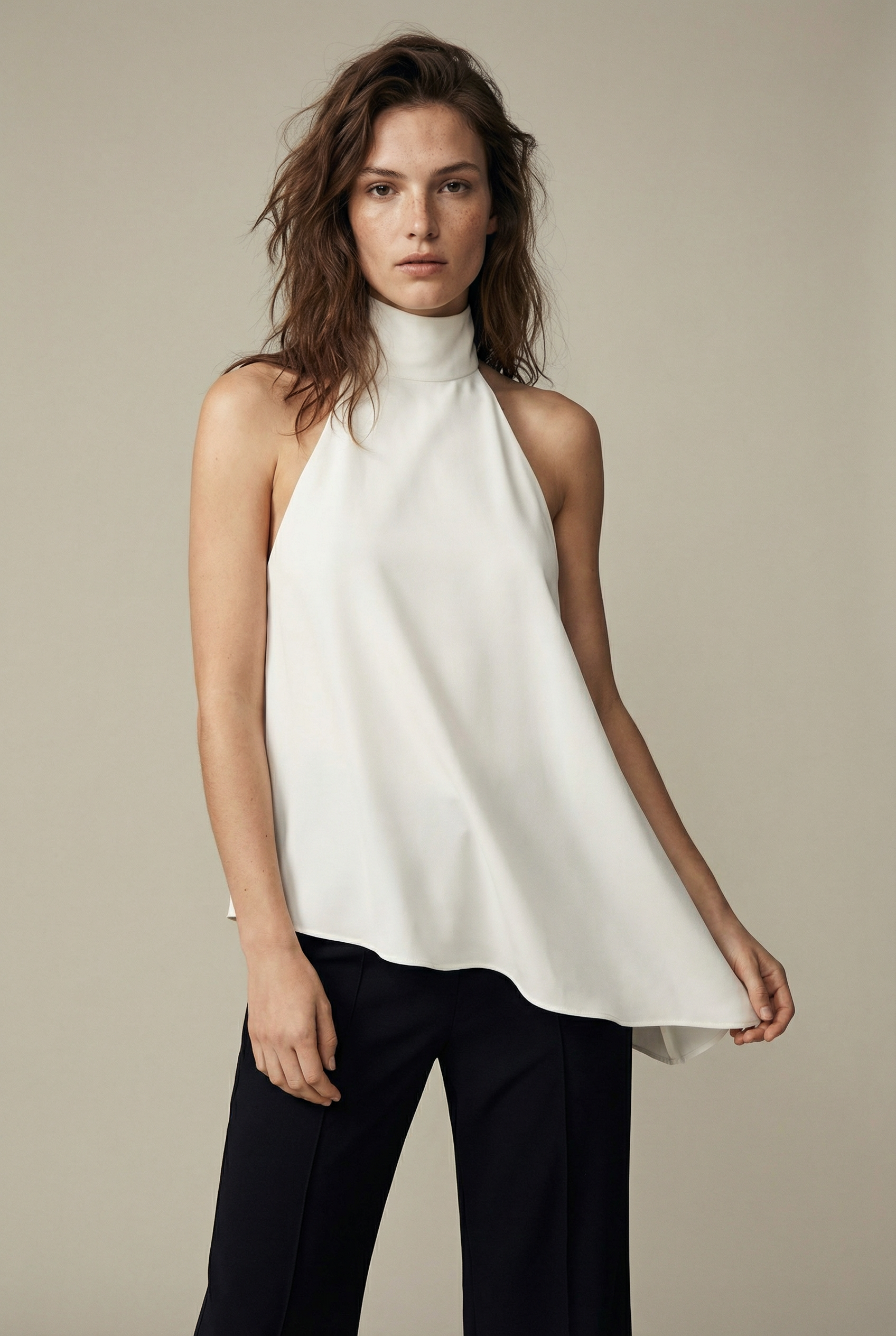 Femme posant avec un haut chic écru, coupe fluide et asymétrique, pour un look contemporain.