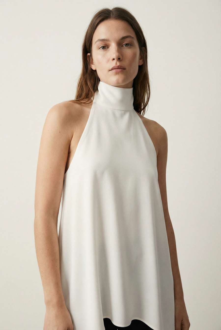Femme avec un haut chic écru, affichant une allure sophistiquée dans un décor simple.
