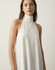 Femme avec un haut chic écru, affichant une allure sophistiquée dans un décor simple.