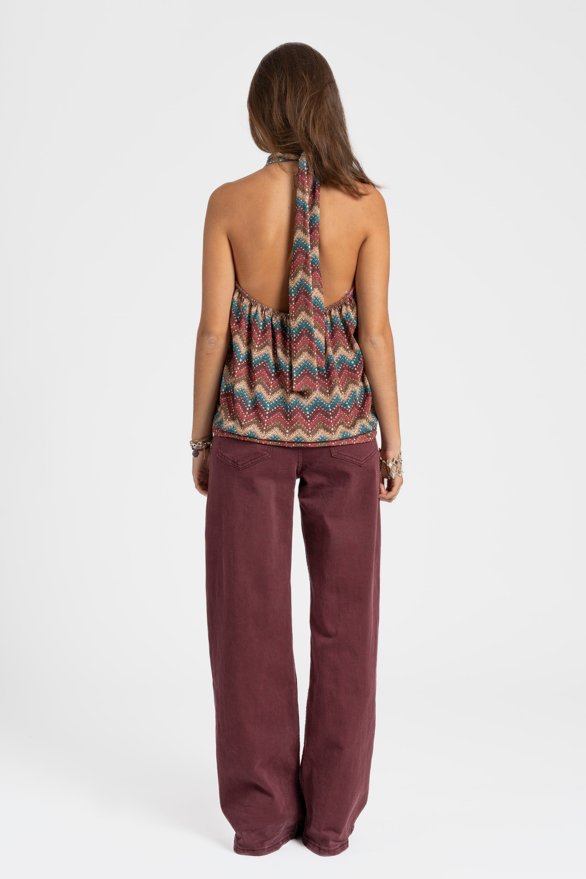 Vue arrière d'une modèle portant un top halter imprimé femme coloré, avec un pantalon large bordeaux.