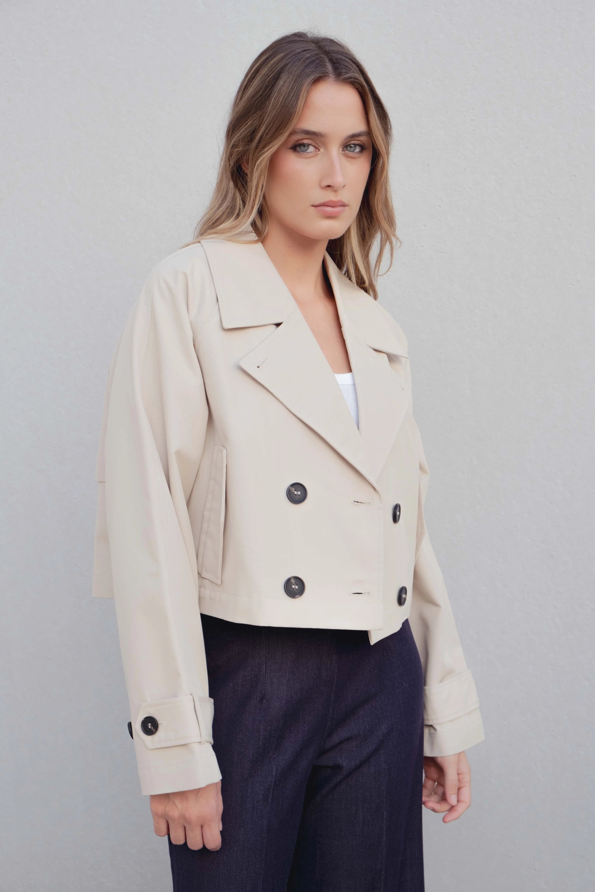 Modèle en portrait portant un trench coat court femme beige à double boutonnage, mettant en valeur la silhouette et le style contemporain.