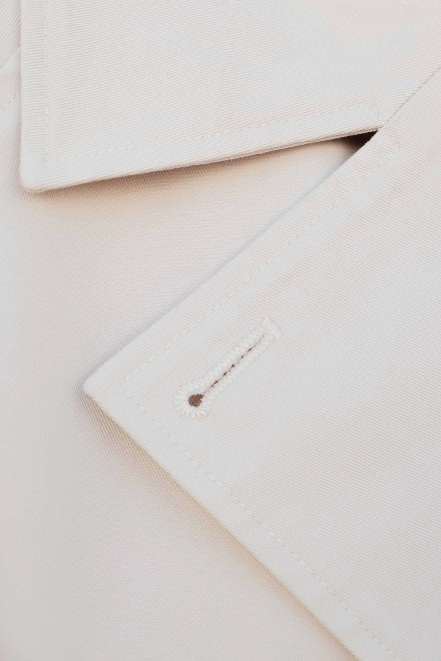 Détail du tissu d'un trench coat court femme beige à double boutonnage, soulignant la qualité et le design élégant de la pièce.