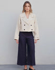Vue de face d'un trench coat court femme beige à double boutonnage, associé à un pantalon large, idéal pour un style élégant et moderne.