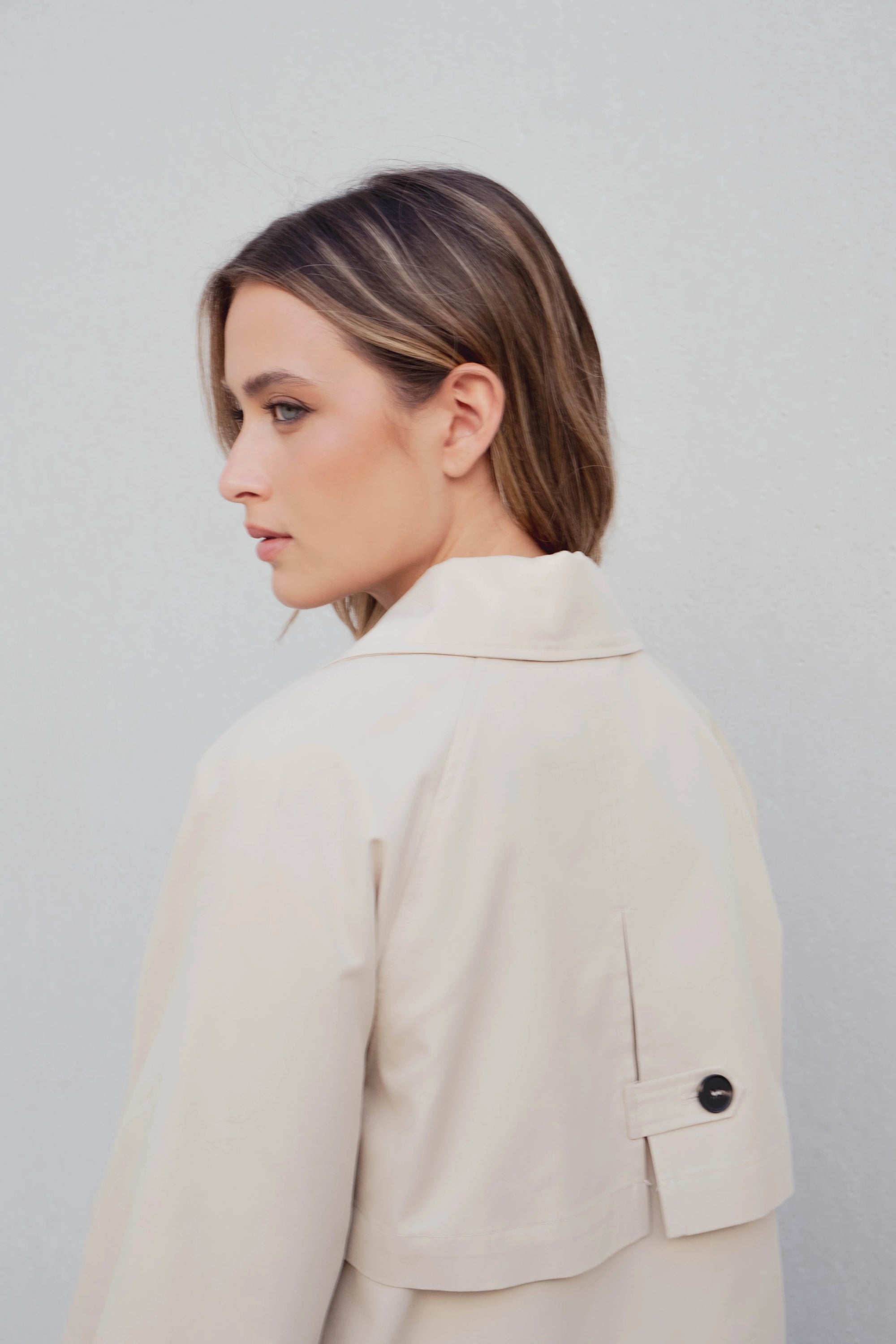 Vue arrière d'un modèle avec un trench coat court femme beige à double boutonnage, mettant en avant le style et la sophistication de la coupe.