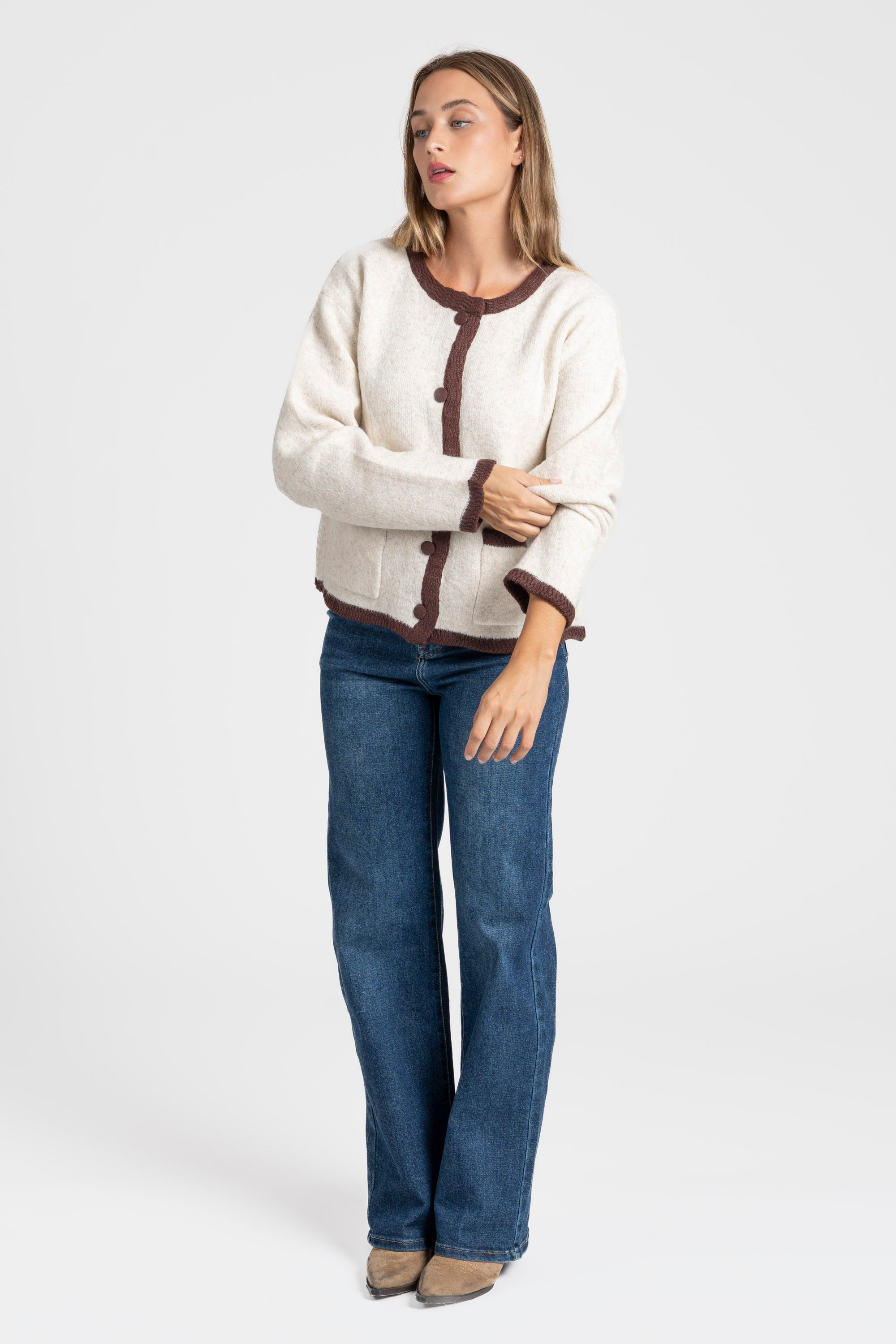 Veste en maille contrastée chic – Coupe droite – Beige ou gris – Maille laine mélangée, montrant une femme assise avec style, combinée avec un jean.