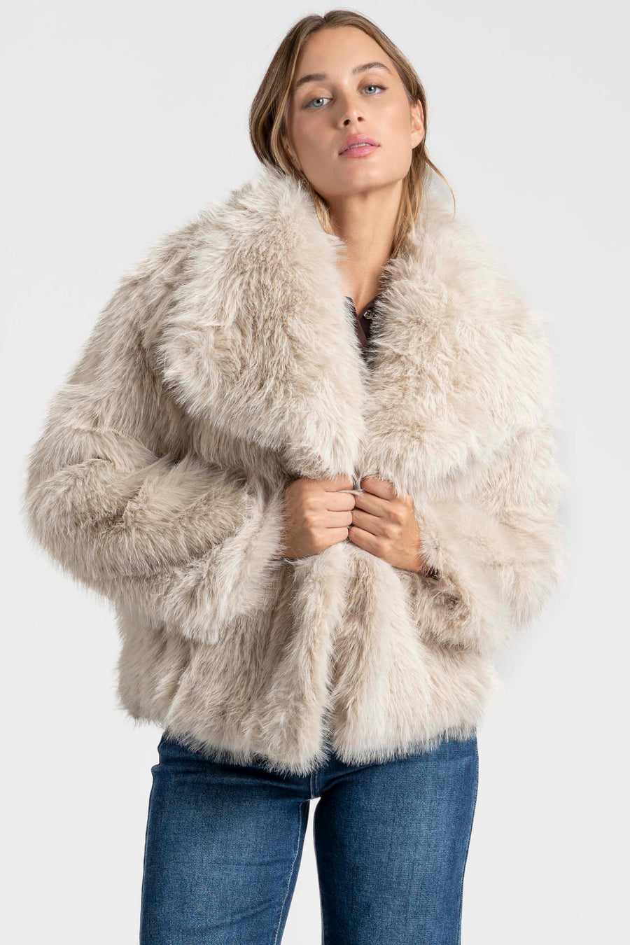 Femme portant une Veste fausse fourrure beige, créant un look élégant avec un pantalon en denim.