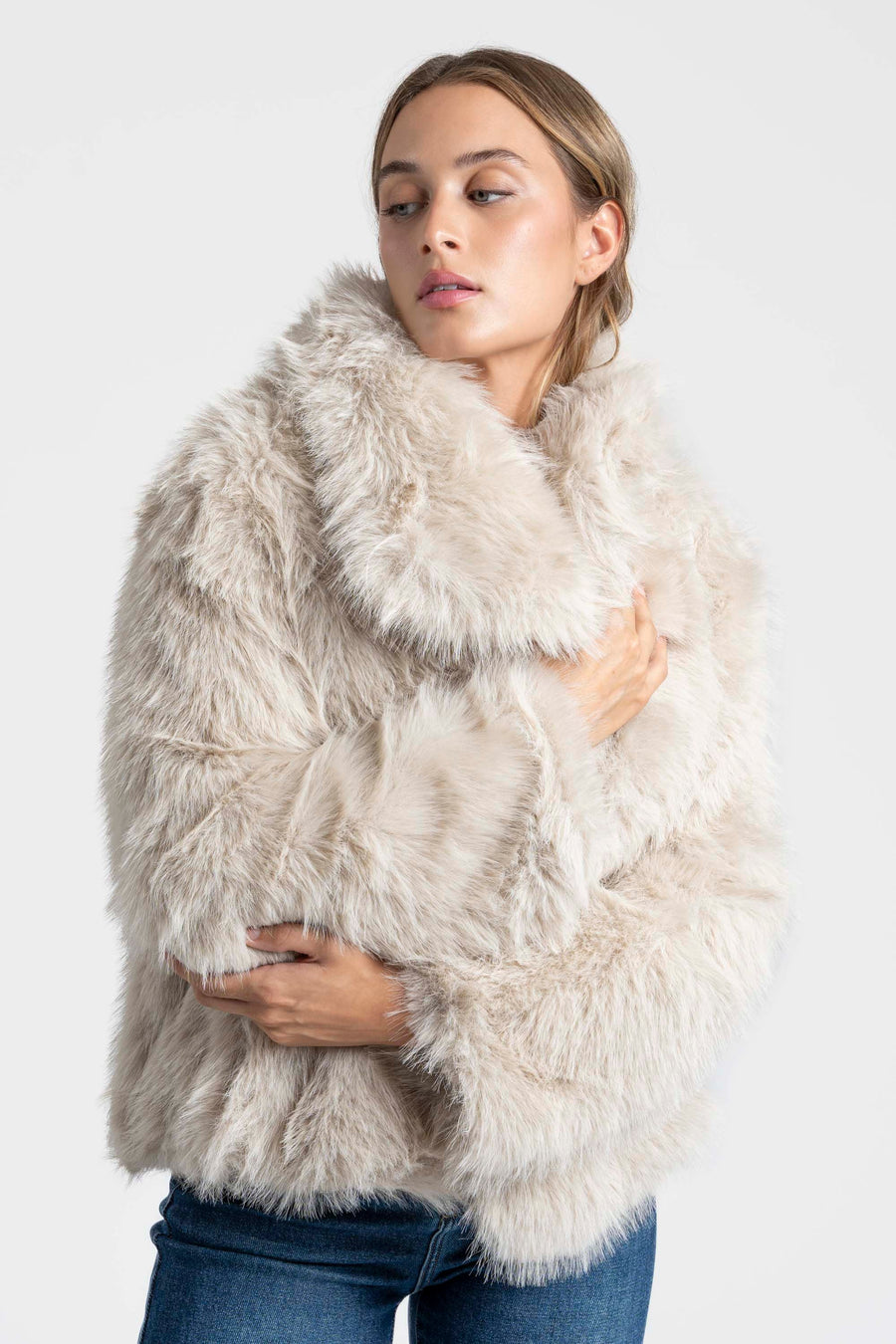Modèle féminin vêtu d'une Veste fausse fourrure beige, avec un col ample, idéale pour une tenue chic et décontractée.