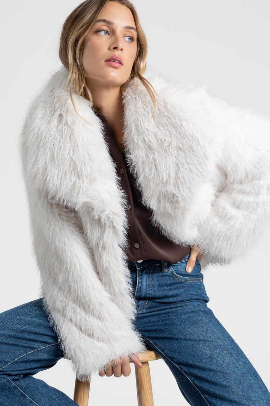 Femme en Veste fausse fourrure blanche, assise avec un style décontracté, parfaite pour la mi-saison.
