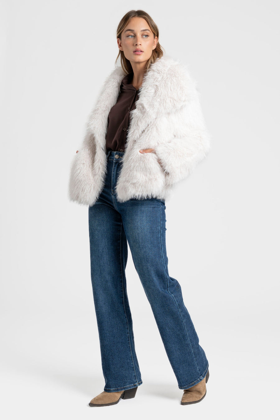 Modèle féminin en Veste fausse fourrure blanche, associée à un look chic contemporain, positionnée debout.