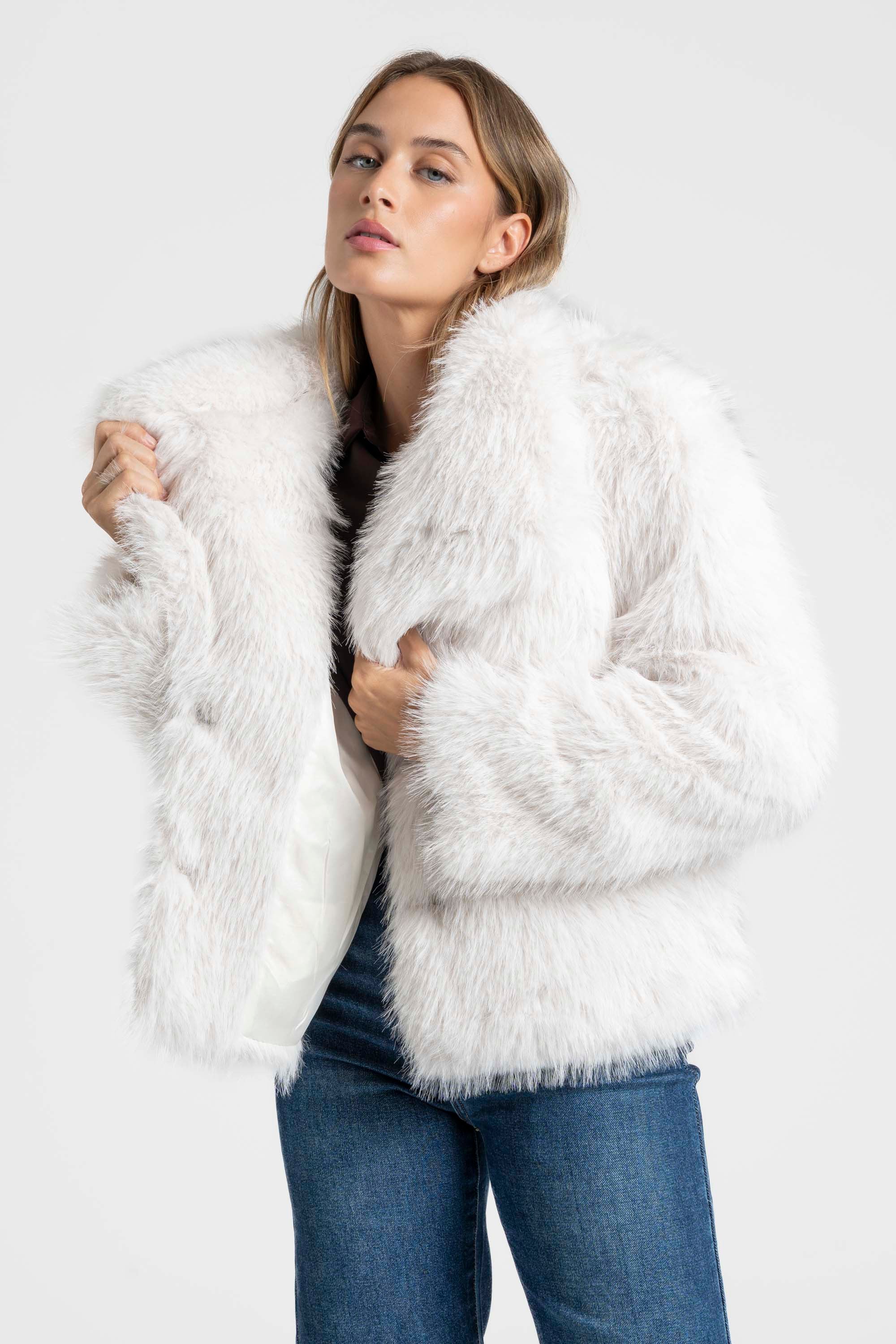 Femme portant une Veste fausse fourrure blanche, affichant une silhouette élégante en posant légèrement de côté.