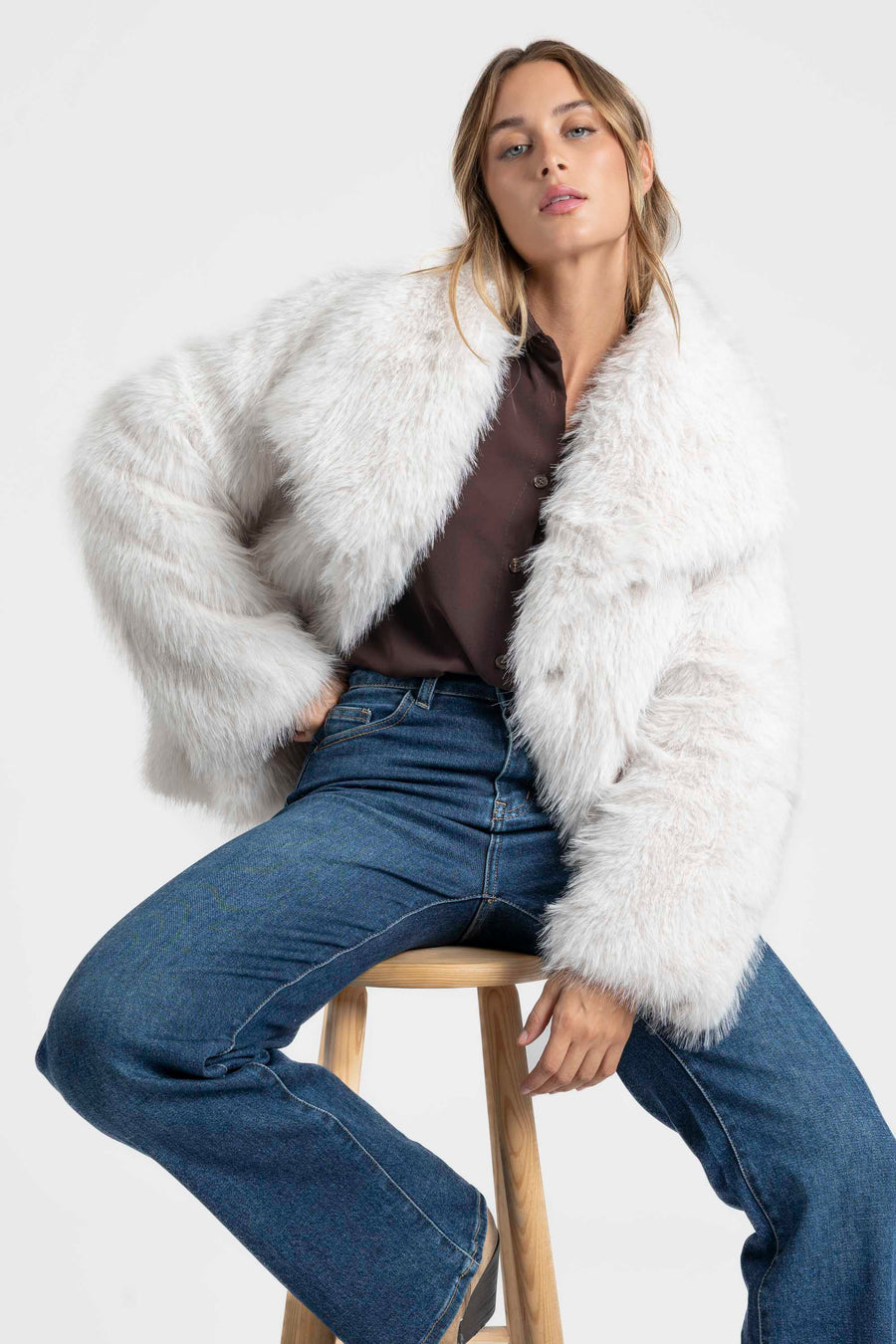 Femme dans une Veste fausse fourrure blanche, avec un look décontracté mais élégant, assise en attendant.